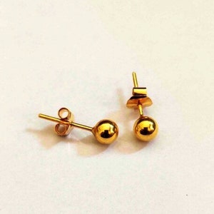 Puede incluir: Un par de pendientes de bola de oro. Los pendientes son simples y elegantes, y serían un gran regalo para cualquier ocasión.