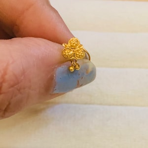 May include: A gold nose ring with a flower design and three small beads hanging from the bottom.