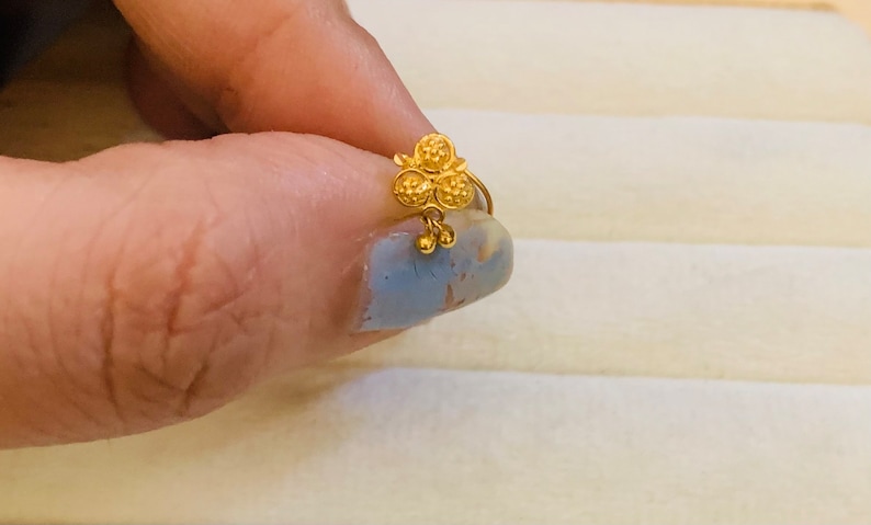 May include: A gold nose ring with a flower design and three small beads hanging from the bottom.