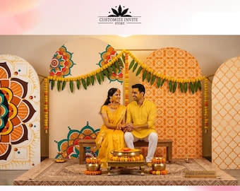 May include: A decorative event backdrop featuring four arched panels with orange and teal mandala patterns, adorned with yellow marigold garlands and green leaves. A wooden bench sits in front, with brass bowls and a small table for Haldi celebrations.