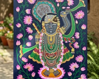 May include: A painting on canvas featuring a dark blue background with a central figure of a deity adorned in intricate gold and green jewelry and clothing. The figure is surrounded by a symmetrical pattern of pink lotus flowers and green vines.