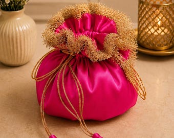 May include: A vibrant fuchsia satin drawstring pouch featuring a gathered top edge adorned with intricate gold metallic mesh trim. The bag includes long, thin gold cord drawstrings that terminate in two matching fuchsia satin fabric tassels.