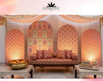 May include: A daybed with a coral and white lattice pattern, featuring matching bolster pillows and cushions. Behind it are four arched panels with intricate floral and geometric prints. Two low tables hold a brass bowl and stacked books.