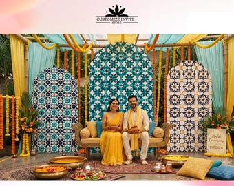 May include: A wedding stage setup featuring three arched backdrops with blue and white geometric patterns, draped yellow and turquoise fabric, marigold garlands, and a gold sofa. A couple sits on the sofa, with brass bowls and a sign reading Haldi Ceremony.
