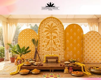 May include: A wedding stage setup featuring four arched yellow backdrops with white patterns, including a central panel with a palm tree and bird motif. A wooden platform holds a small bench, brass bowls with offerings, and marigold garlands.