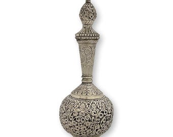 May include: A silver-toned metal bottle with a rounded base and a long, slender neck topped with a pointed, decorative stopper. The entire surface is covered in intricate, embossed floral and leaf patterns with dark, recessed detailing.