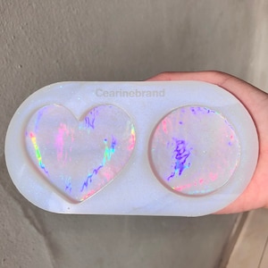 May include: White silicone mould with two cavities, one heart-shaped and one round. The mould is filled with iridescent resin, creating a shimmering effect.