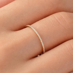 May include: A delicate gold ring with a thin band, adorned with small, sparkling gemstones. The ring is shown on a finger, highlighting its elegant and minimalist design. A piece of jewelry suitable for everyday wear or special occasions.