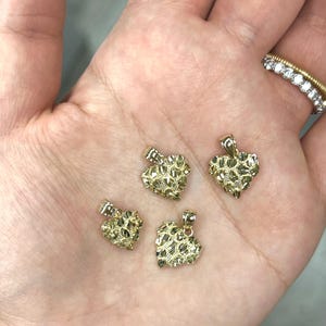 May include: Four gold heart-shaped pendants with a textured diamond-cut finish. The pendants are of varying sizes and are displayed on a hand.