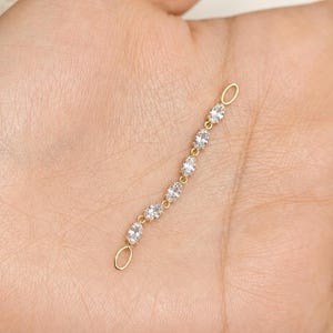 May include: A gold-toned jewelry connector chain featuring six small, clear, oval-shaped faceted stones set in a vertical row. The delicate chain has a small, plain gold-toned oval loop at both the top and bottom ends for attachment purposes.