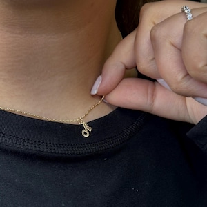 Op de afbeelding: Een delicate gouden ketting met een hanger in de vorm van een cursieve letter "A". De hanger hangt aan een fijne gouden ketting. De ketting wordt getoond tegen een zwarte achtergrond.