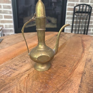 May include: A brass teapot with an ornate design and a hinged lid. The teapot has a spout and a handle.