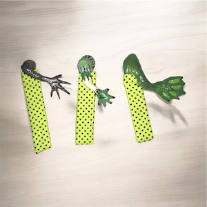 May include: Three green frog bookmarks with black polka dot fabric. Each bookmark features a different frog limb, including a hand, an arm, and a tail.