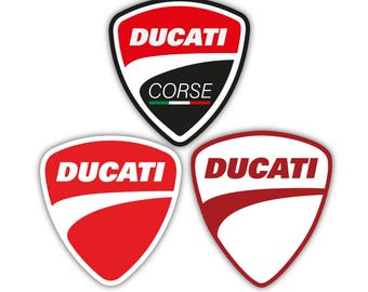 May include: Three Ducati logo stickers. The top sticker is a shield shape with the word "DUCATI" in white on a red background, and "CORSE" on a black background. The other two stickers are red and white shield shapes with the word "DUCATI".