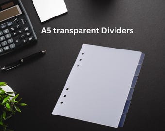 May include: A5 transparent dividers with blue tabs, arranged on a black surface. The dividers have pre-punched holes for binding. A calculator, pen, and a small white card are also visible.