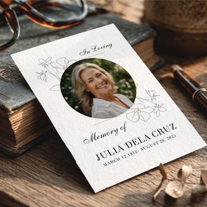 May include: A memorial card with the text "In Loving Memory of JULIA DELA CRUZ MARCH 12, 1972- AUGUST 20, 2023." The card features a circular photo of a smiling woman and floral line art.