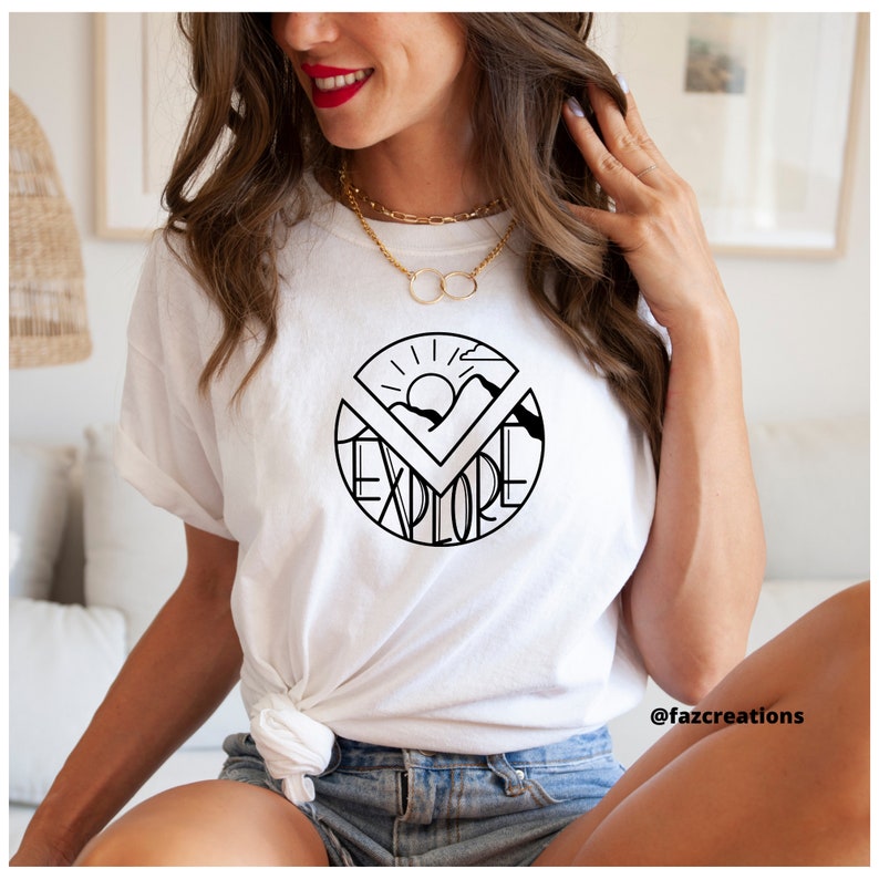 May include: White t-shirt with a black graphic of a sun, mountains, and the word "explore" in a circle.