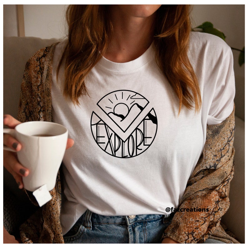 May include: White t-shirt with a black graphic design of a sun, mountains, and the word "explore" in a circle.