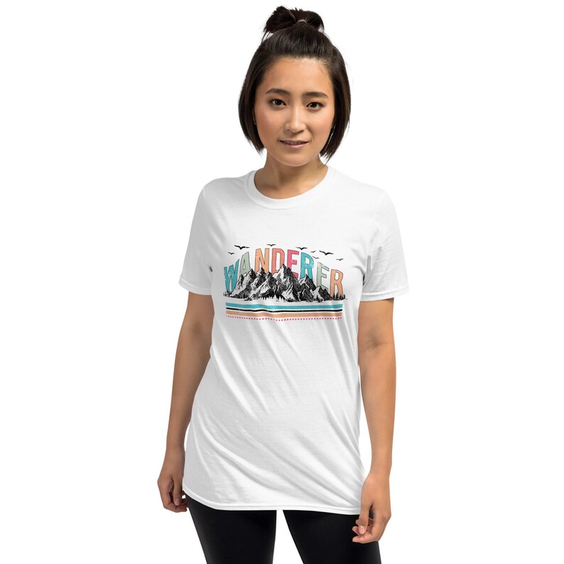 May include: White t-shirt with a graphic of mountains and the word "WANDERER" in colorful letters.