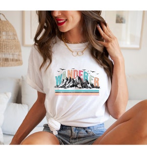 May include: White t-shirt with a colorful graphic of mountains and the word "WANDERER" printed on it.