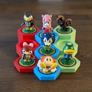 May include: A hexagonal display stand with six compartments, each featuring a different Animal Crossing character figurine. The characters include a red owl, a pink sheep, a brown bear, a blue wolf, a green frog, and a pink and yellow Kirby.