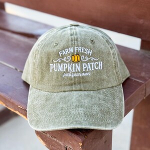 May include: A green baseball cap with the text "Farm Fresh Pumpkin Patch pick your own" embroidered in white. A small orange pumpkin with a yellow stem is embroidered above the text.