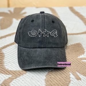 May include: A black denim baseball cap with white embroidered seashells and a starfish. The text "Embroidered" is on the bill of the cap.