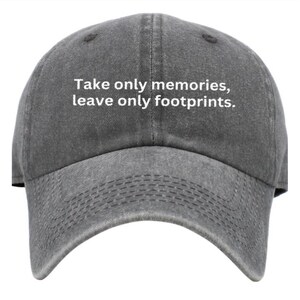 以下が含まれることがあります： 白い刺繍で「Take only memories, leave only footprints.」と書かれた灰色のベースボールキャップ