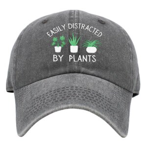 May include: A gray baseball cap with the text "Easily Distracted By Plants" embroidered on the front. Three green potted plants are depicted below the text.