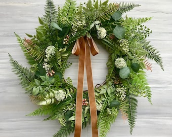 May include: A green and brown wreath made of ferns and eucalyptus leaves with a brown velvet ribbon.