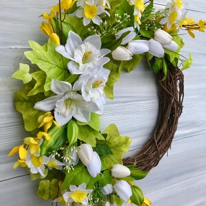 May include: A spring wreath with white and yellow flowers, green leaves, and a brown vine base.