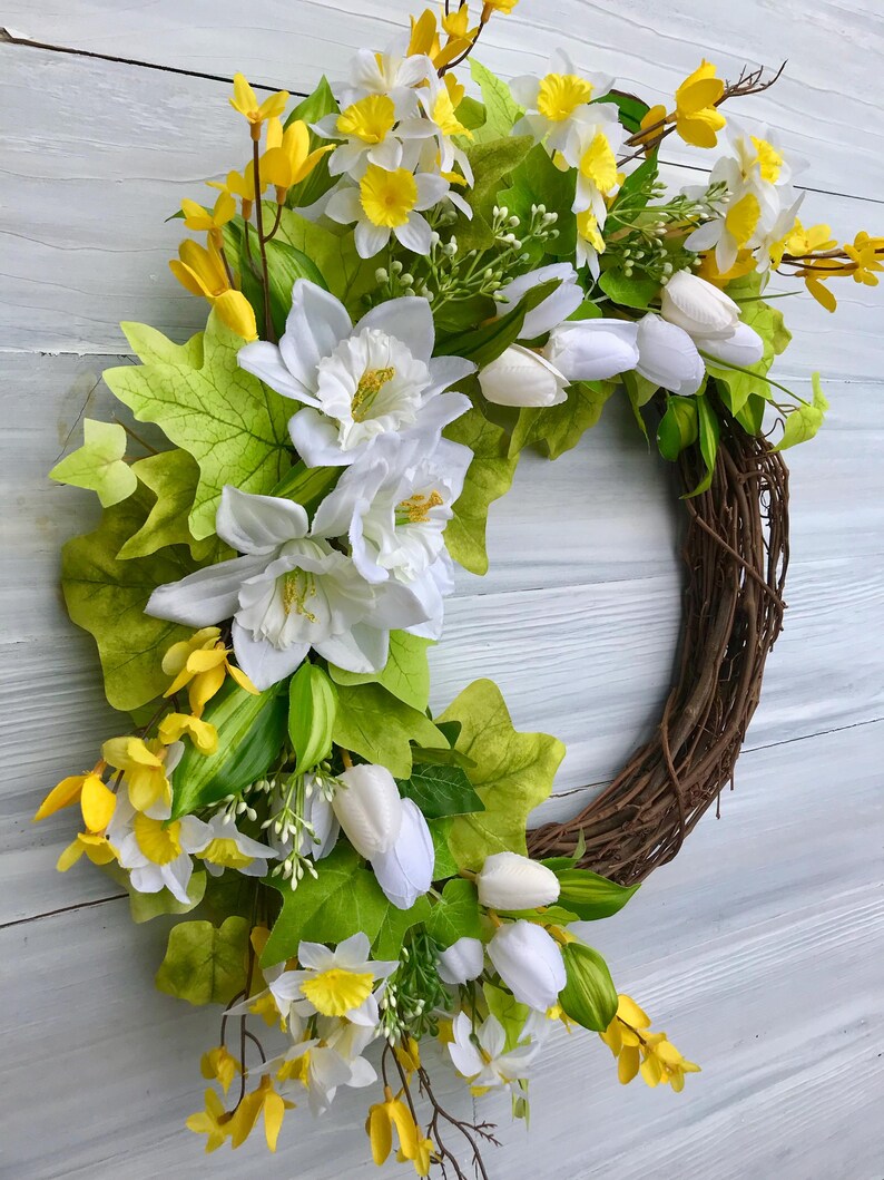 May include: A spring wreath with white and yellow flowers, green leaves, and a brown vine base.