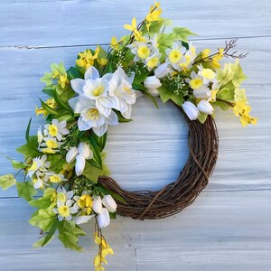 May include: A spring wreath with white and yellow flowers, including daffodils and tulips, on a brown vine base.