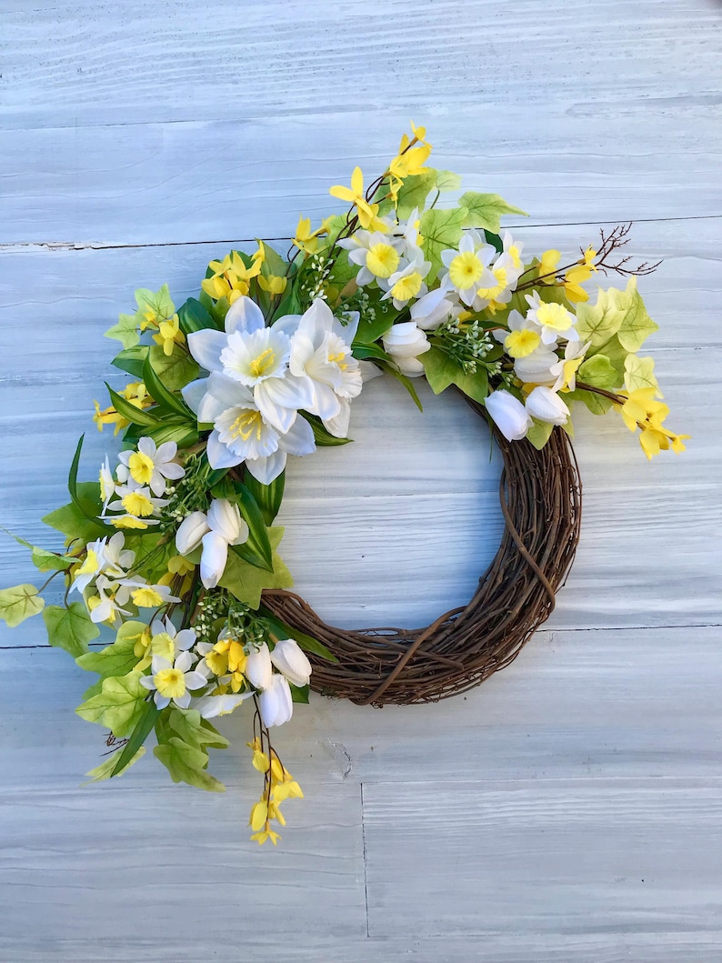 May include: A spring wreath with white and yellow flowers, including daffodils and tulips, on a brown vine base.