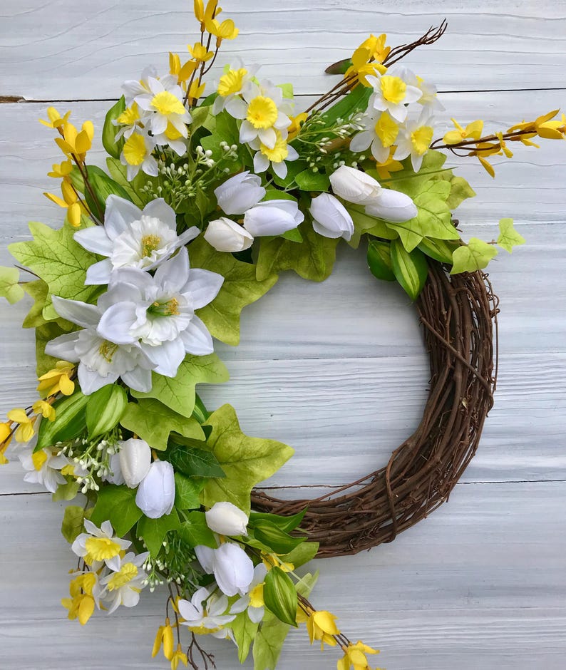 May include: A spring wreath with white tulips, yellow daffodils, and green leaves on a brown vine base.