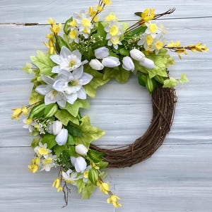 May include: A spring wreath with white tulips, yellow daffodils, and green leaves on a brown vine base.