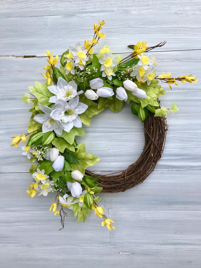 May include: A spring wreath with white tulips, yellow daffodils, and green leaves on a brown vine base.