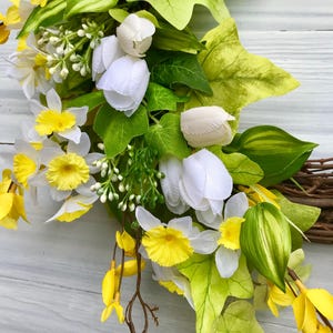 May include: A spring wreath with white tulips, yellow daffodils, and green leaves.