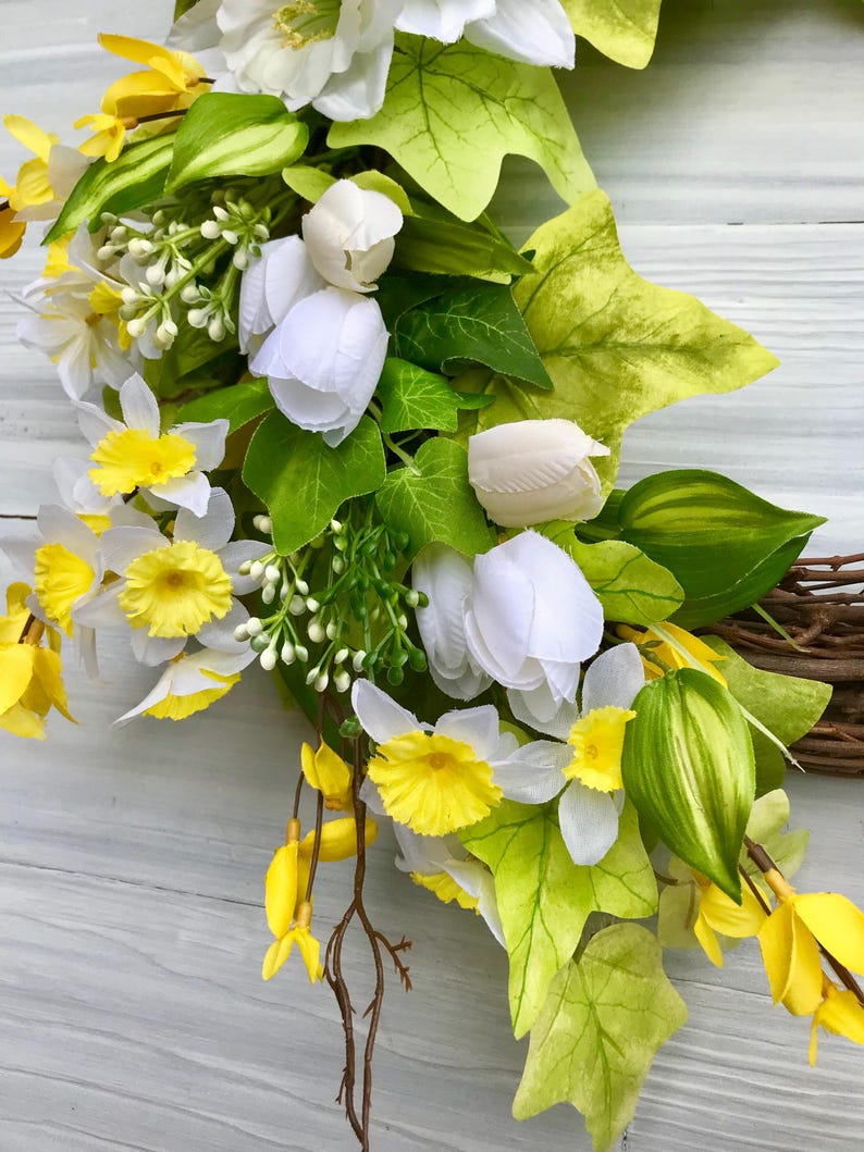 May include: A spring wreath with white tulips, yellow daffodils, and green leaves.