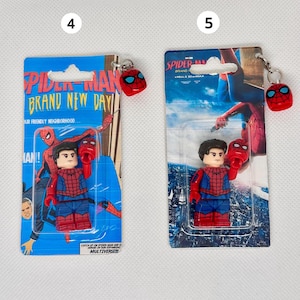 Op de afbeelding: Twee Spider-Man sleutelhangers. Elke sleutelhanger heeft een kleine Spider-Man figuur en een rode Spider-Man masker bedel. De verpakking leest "Spider-Man Brand New Day" en "Catch up on Spider-Man and Heroes in our expanding Multiverse!!!"