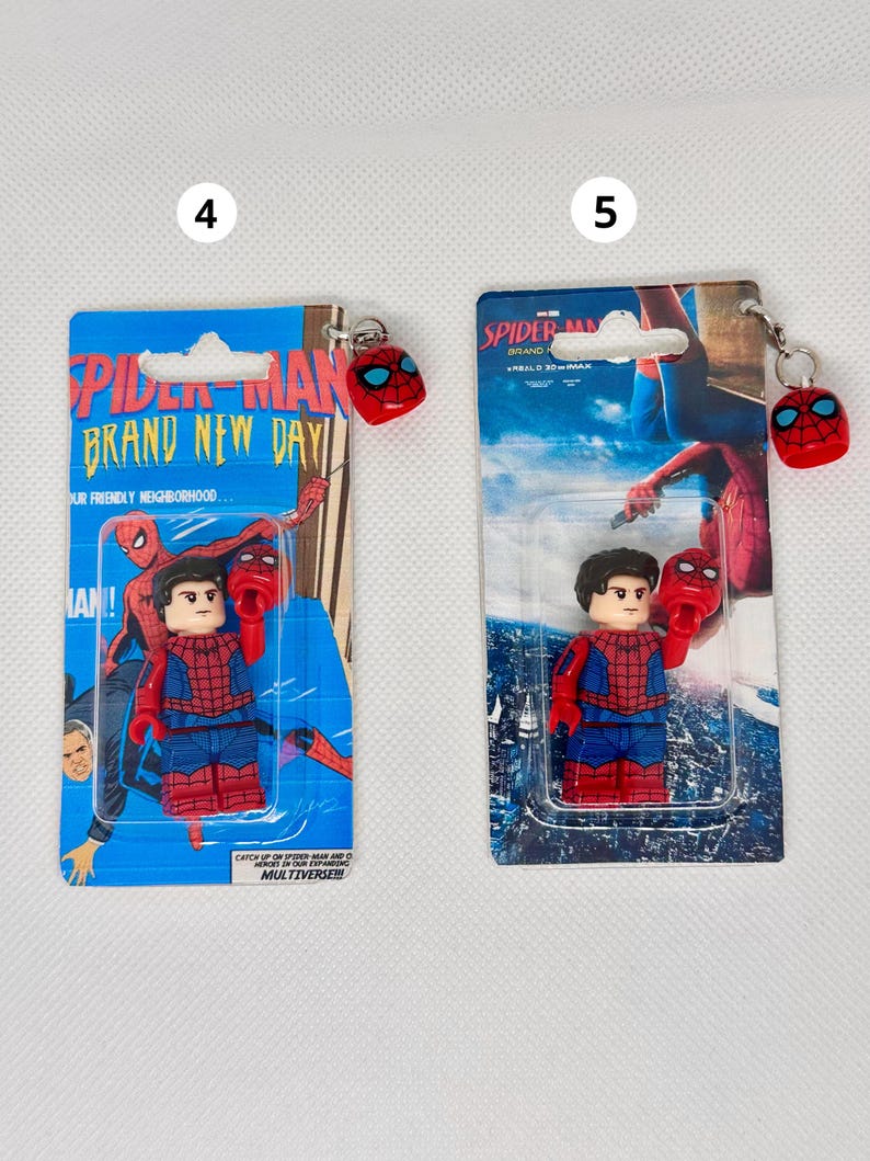 Op de afbeelding: Twee Spider-Man sleutelhangers. Elke sleutelhanger heeft een kleine Spider-Man figuur en een rode Spider-Man masker bedel. De verpakking leest "Spider-Man Brand New Day" en "Catch up on Spider-Man and Heroes in our expanding Multiverse!!!"