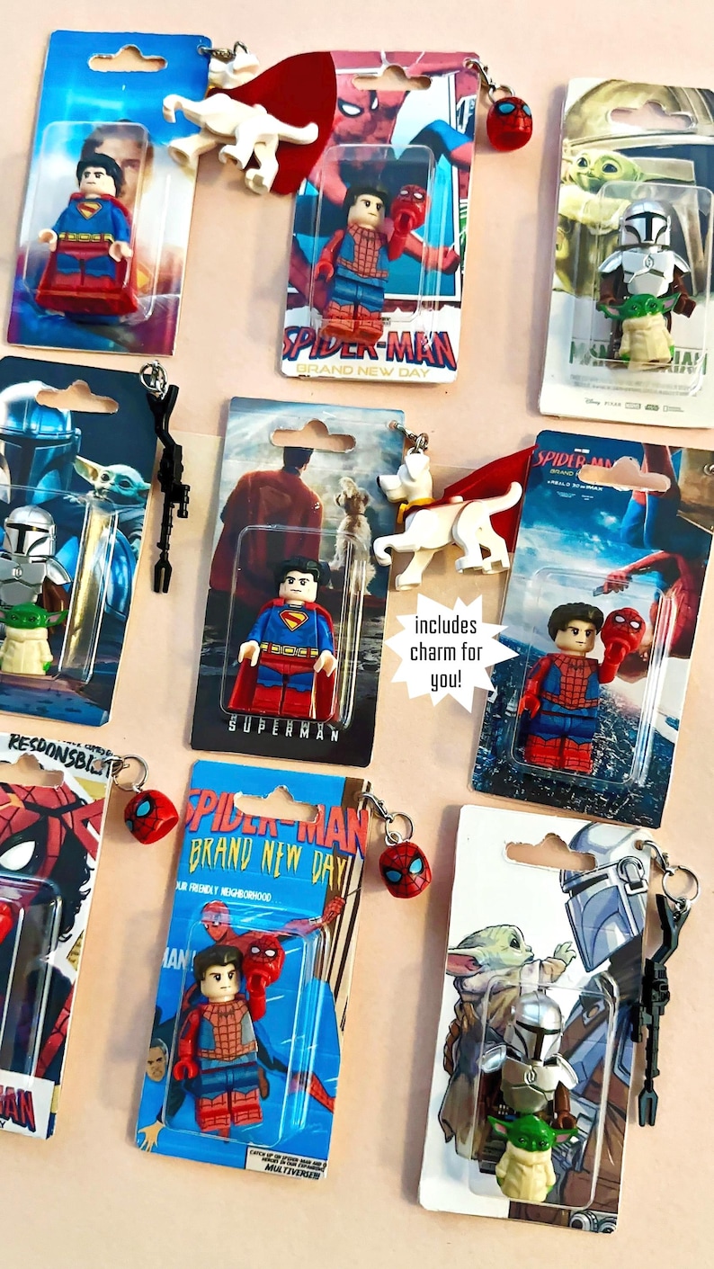 Op de afbeelding: Assortiment van sleutelhangers met superhelden, met personages als Superman, Spider-Man en The Mandalorian. Elke sleutelhanger bevat een kleine bedel en is verpakt op een kleurrijke kaart. De tekst "includes charm for you!" is zichtbaar.
