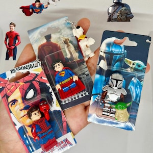 Op de afbeelding: Een verzameling sleutelhangers en beeldjes met superhelden, waaronder Spider-Man, Superman en The Mandalorian. Elke figuur is verpakt op een kaart met merknaam. De afbeelding bevat ook uitsparingen van Superman, Spider-Man en een hond.