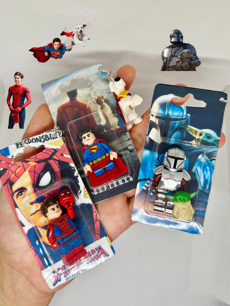 Op de afbeelding: Een verzameling sleutelhangers en beeldjes met superhelden, waaronder Spider-Man, Superman en The Mandalorian. Elke figuur is verpakt op een kaart met merknaam. De afbeelding bevat ook uitsparingen van Superman, Spider-Man en een hond.