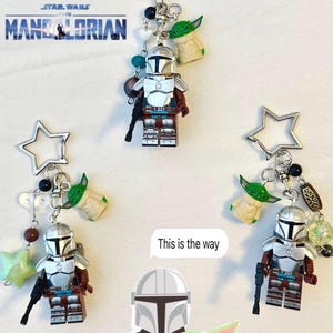May include: Keychains featuring Mandalorian figures and Grogu charms. Each keychain includes a silver star-shaped charm, beads, and a miniature figure of the Mandalorian with a blaster. The text "This is the way" is also visible.