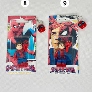Op de afbeelding: Twee Spider-Man sleutelhangers en minifiguren. Elke sleutelhanger heeft een rood Spider-Man masker. De minifiguren dragen rode en blauwe Spider-Man pakken. De verpakking leest "Spider-Man Brand New Day".