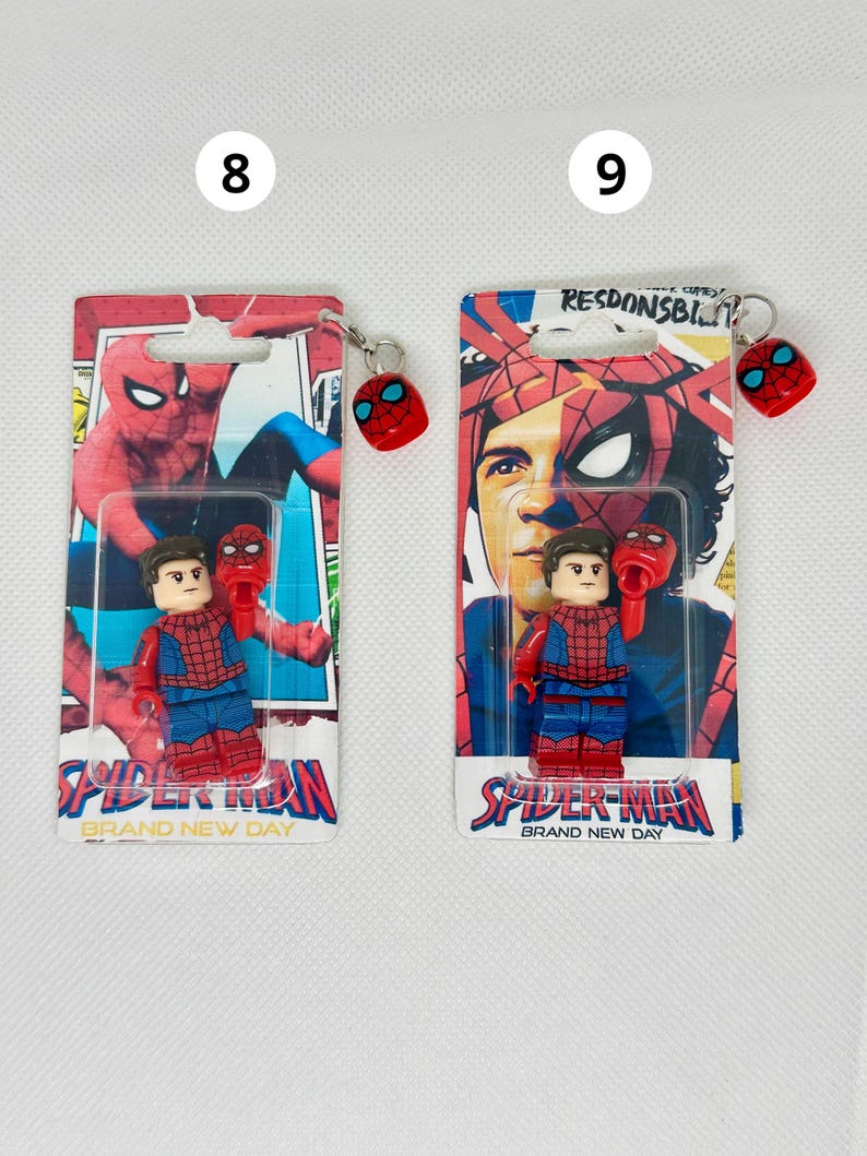 Op de afbeelding: Twee Spider-Man sleutelhangers en minifiguren. Elke sleutelhanger heeft een rood Spider-Man masker. De minifiguren dragen rode en blauwe Spider-Man pakken. De verpakking leest "Spider-Man Brand New Day".