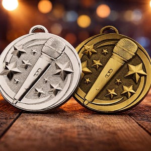 Puede incluir: Dos medallas redondas, una plateada y otra dorada, con un micrófono y estrellas. Están sobre una superficie de madera, con un fondo borroso de luces. Las medallas tienen un lazo en la parte superior para colgar.