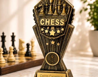 May include: A bronze-toned resin chess trophy featuring a relief of chess pieces and the word CHESS at the top. Below, a circular emblem shows a torch, and the base includes a gold plaque engraved with the text CHESS CHAMPION 2026.