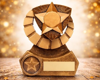 May include: A gold-colored trophy with a star-shaped emblem. The trophy features a star at the top, a circular design, and a rectangular space for personalization. The base has a star emblem and a blank nameplate.